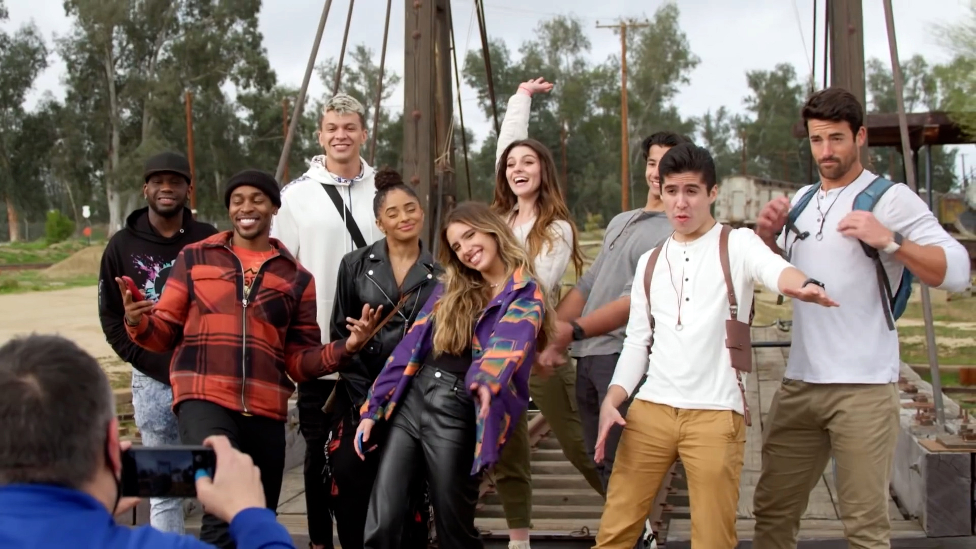 A group of social media influencers stand on a bridge, posing and smiling for a man taking their photo on a phone.
