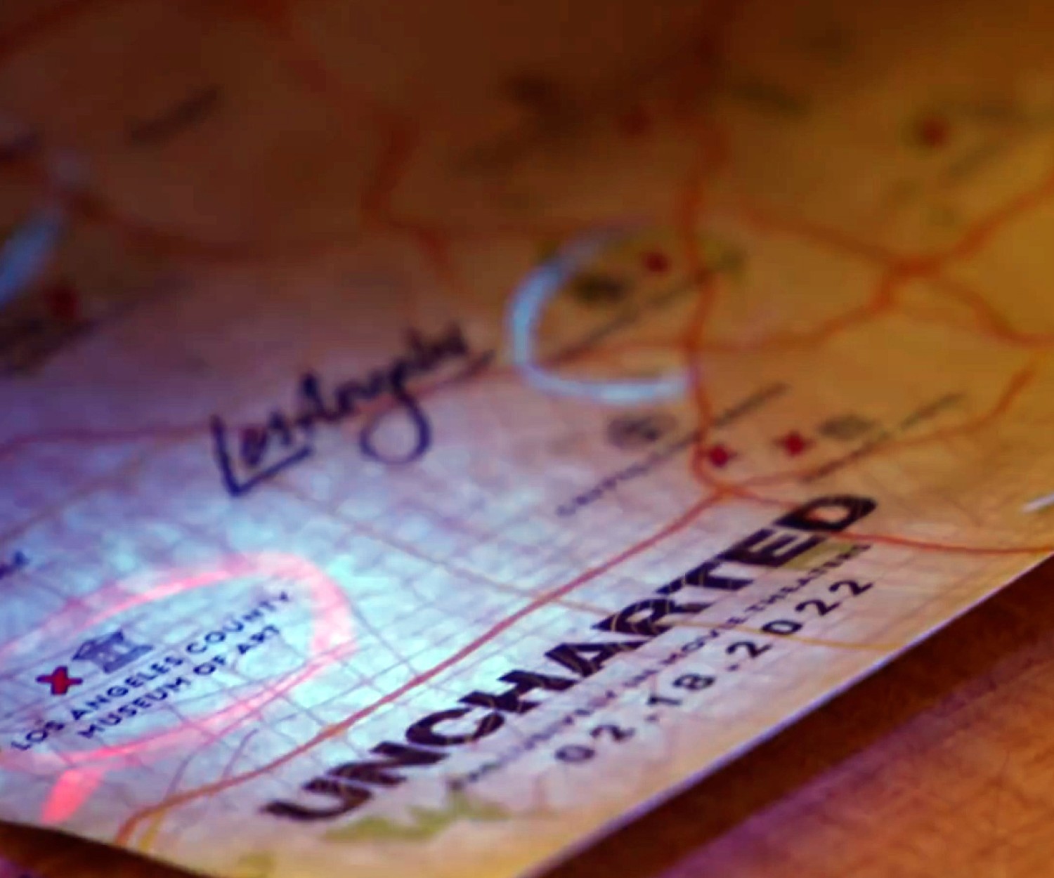 UNCHARTED film logo is seen on a stylized map of Los Angeles. The LA County Museum of Art is circled with a read pen and “2-18-2022” is printed below the logo. A light focuses on the logo.